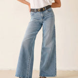 Person wearing blue jeans and a white shirt on a plain background