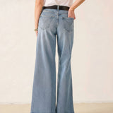 Person wearing light blue wide-leg jeans and a white shirt on a plain background