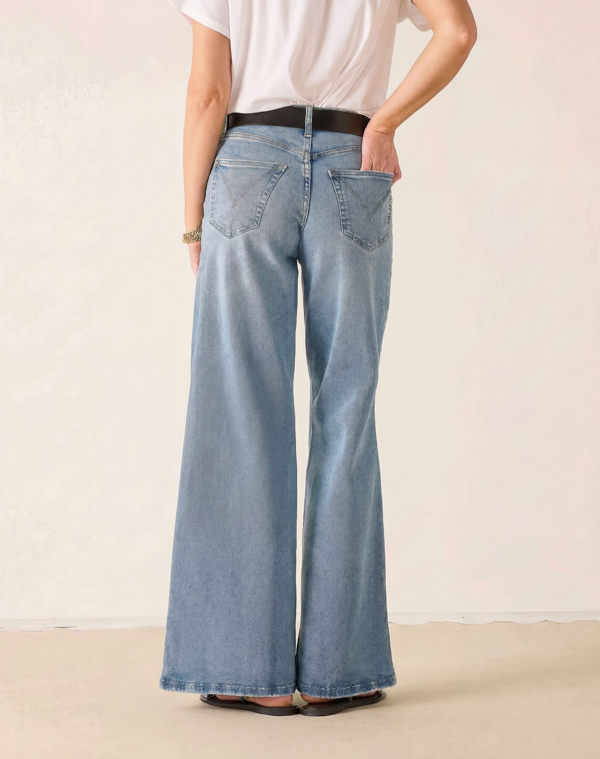 Person wearing light blue wide-leg jeans and a white shirt on a plain background