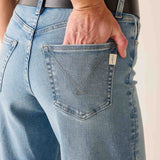 Person wearing blue jeans with a necklace in the pocket against a neutral background