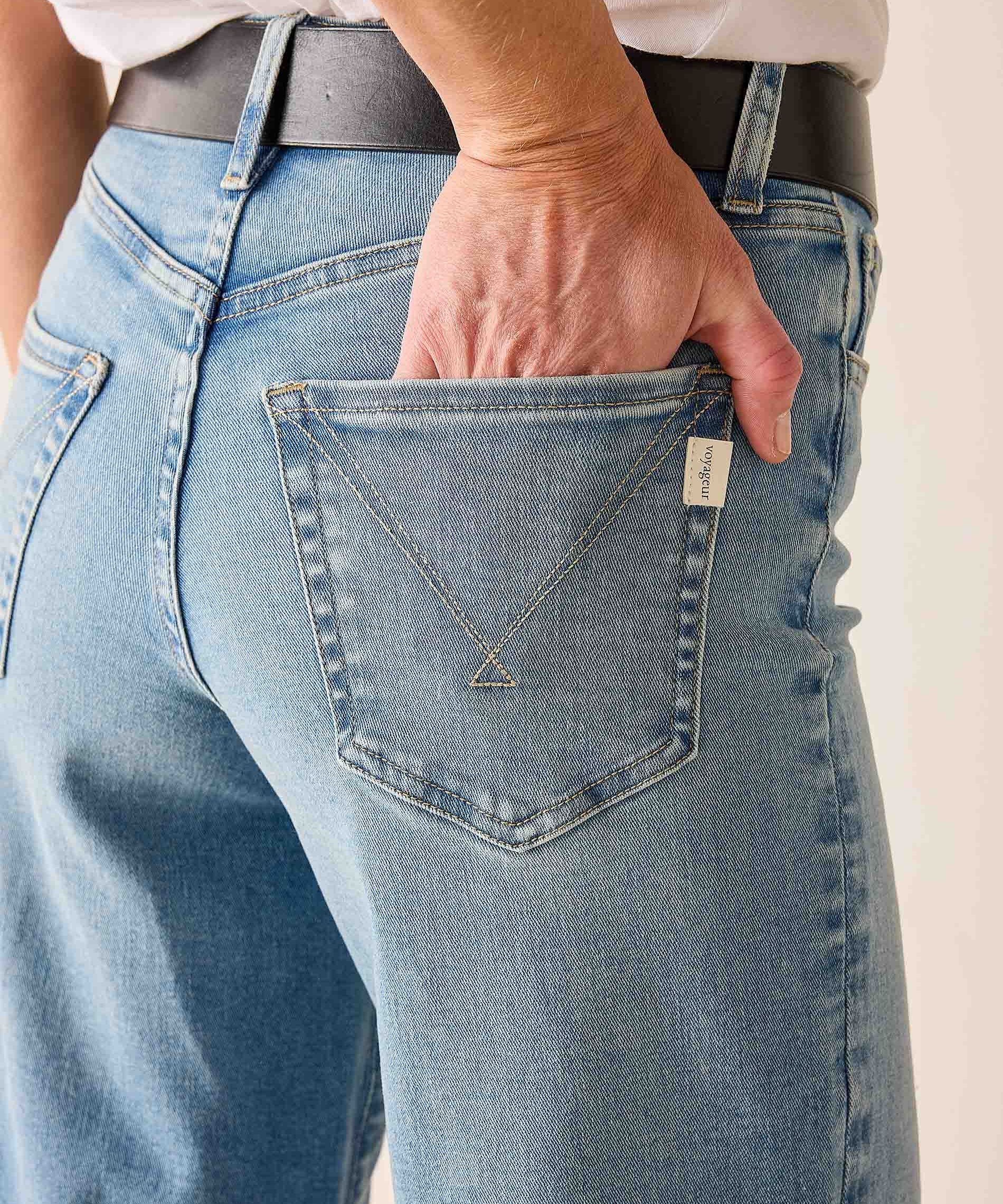 Person wearing blue jeans with a necklace in the pocket against a neutral background