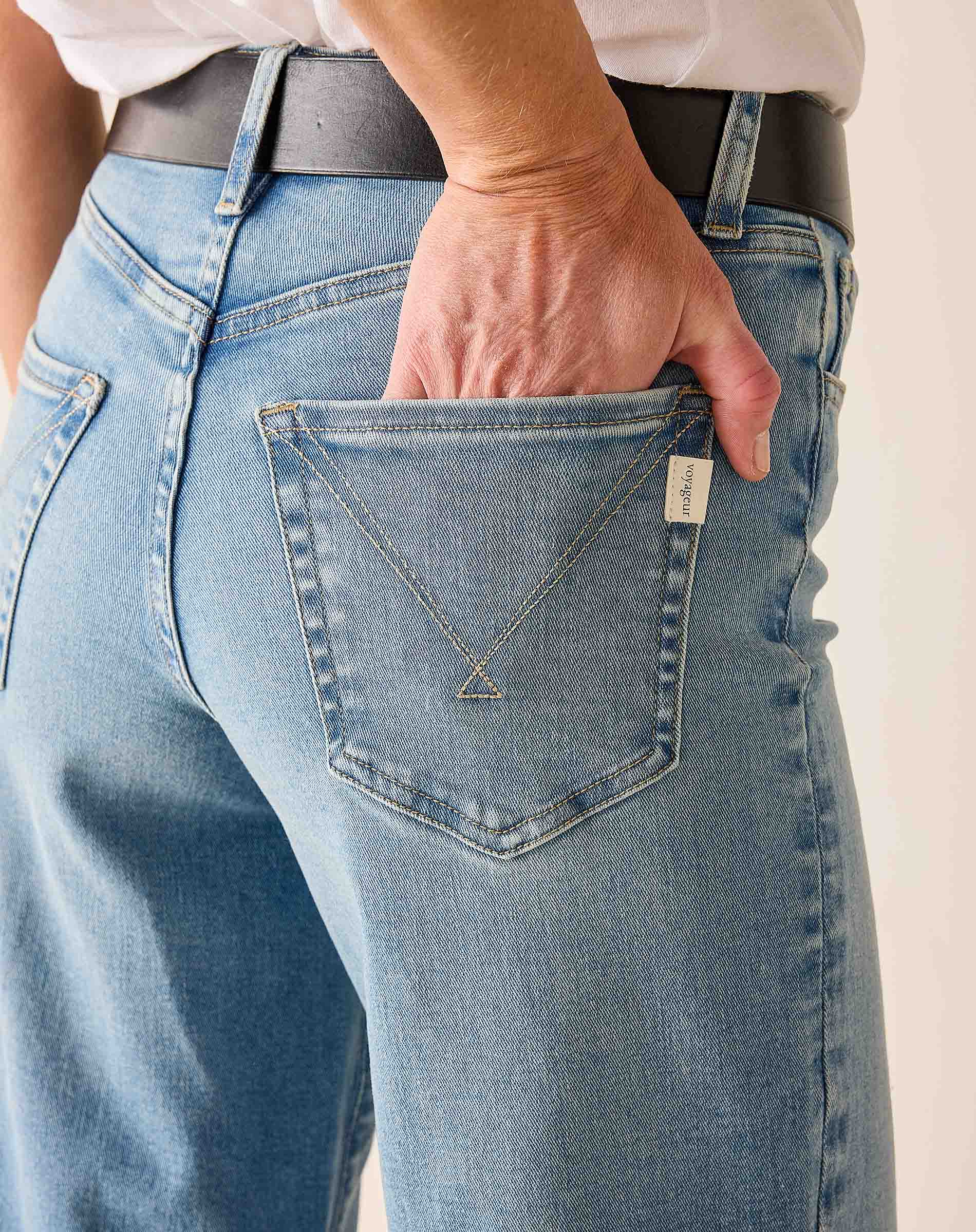 Person wearing blue jeans with a necklace in the pocket against a neutral background