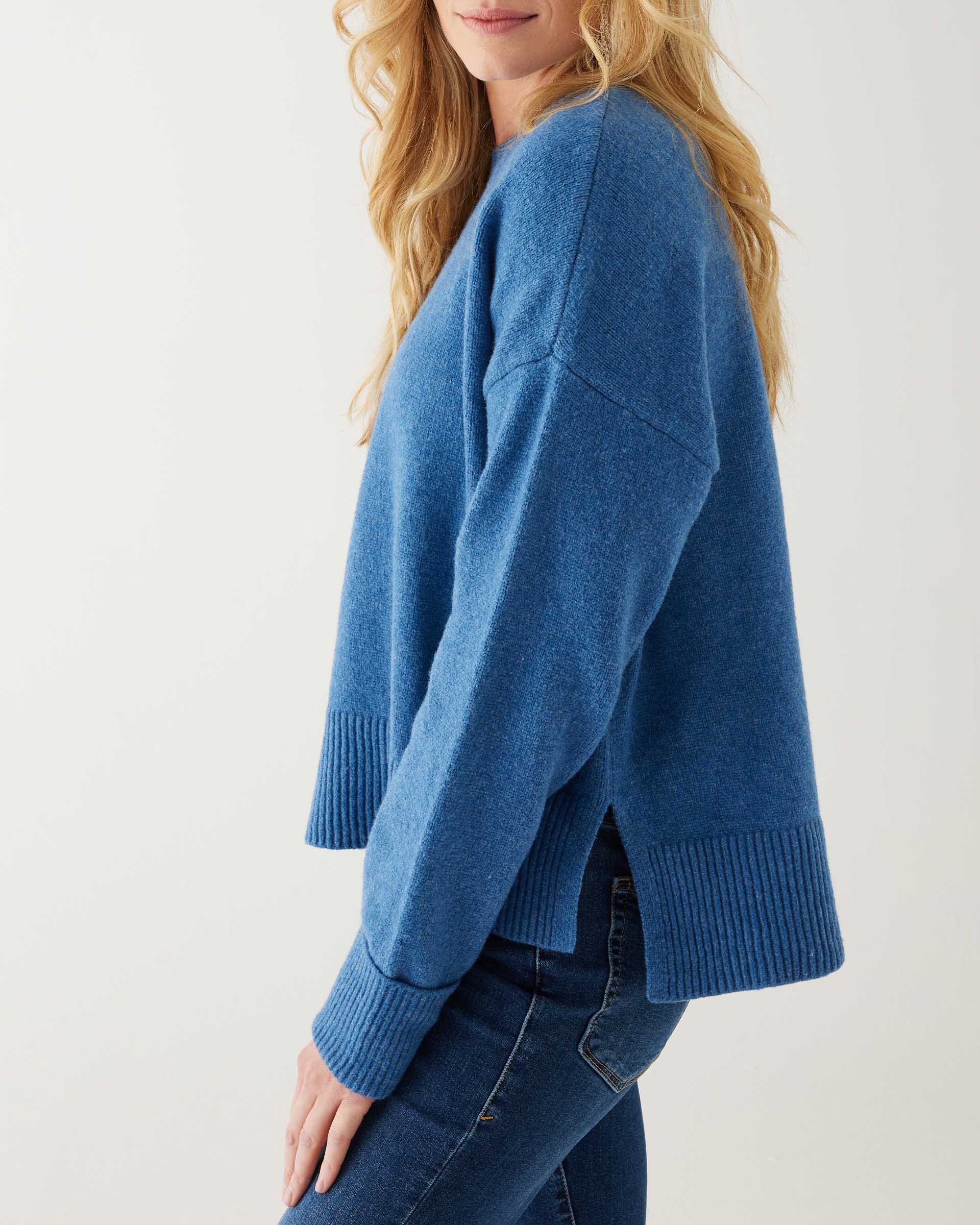 profile of female wearing denim blue crewneck sweater standing in front of a white background