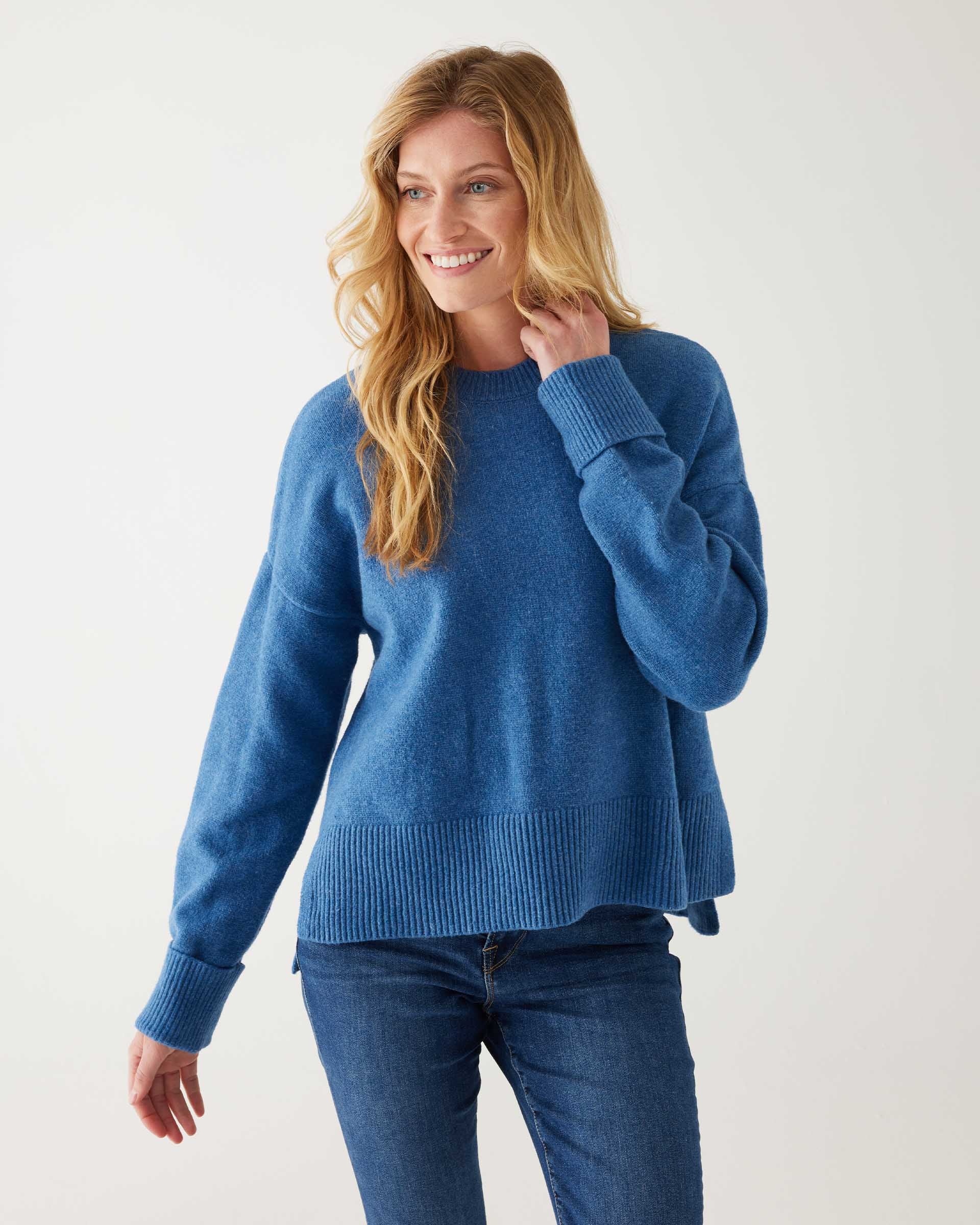 female wearing denim blue crewneck sweater standing in front of a white background