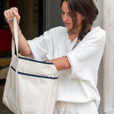 Woman holding a large white tote bag with blue stripes.