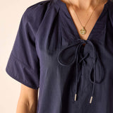 Navy blue blouse with tied sleeves and neckline on a beige background