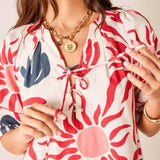 Woman wearing a red and white floral dress with a gold necklace against a neutral background
