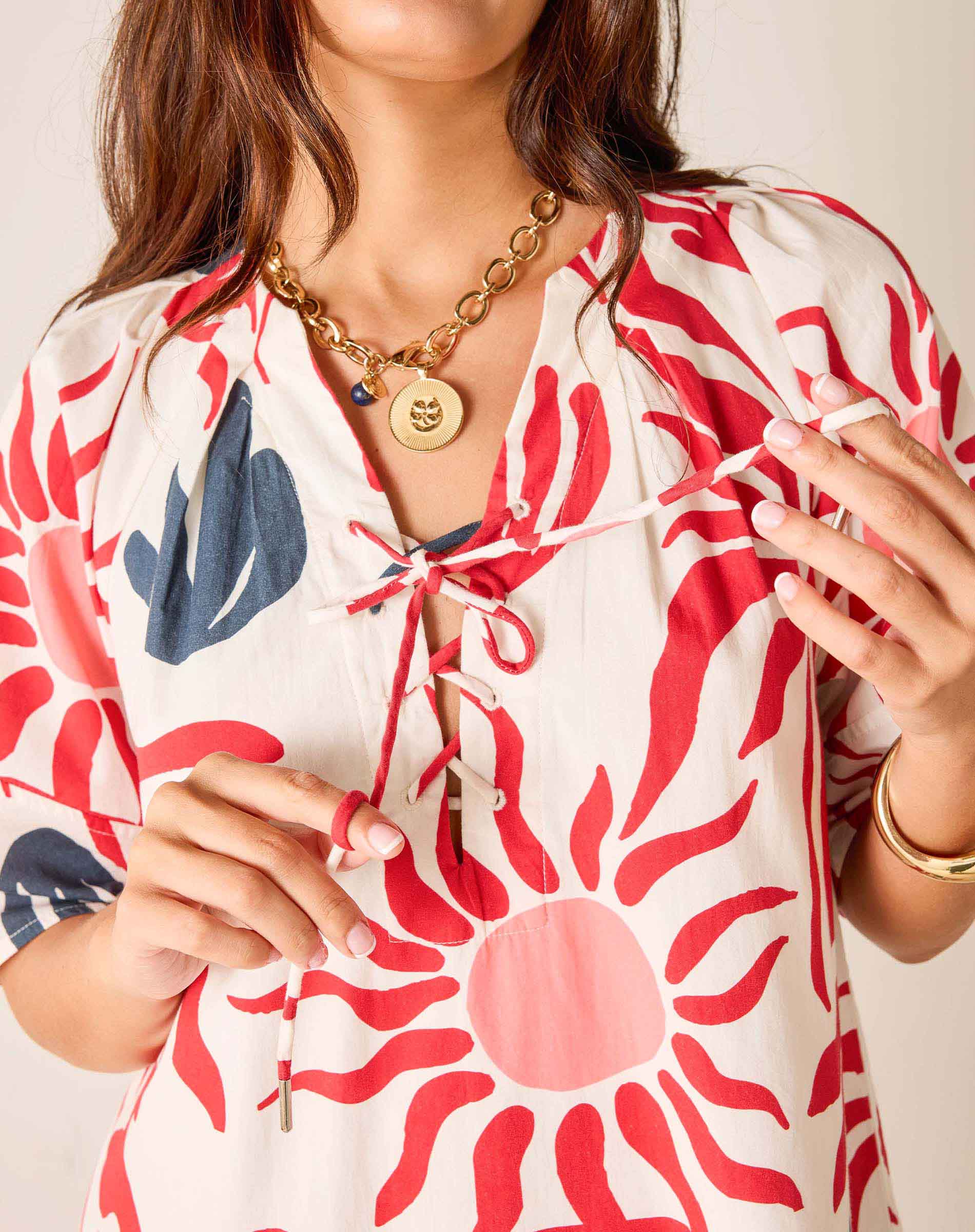 Woman wearing a red and white floral dress with a gold necklace against a neutral background