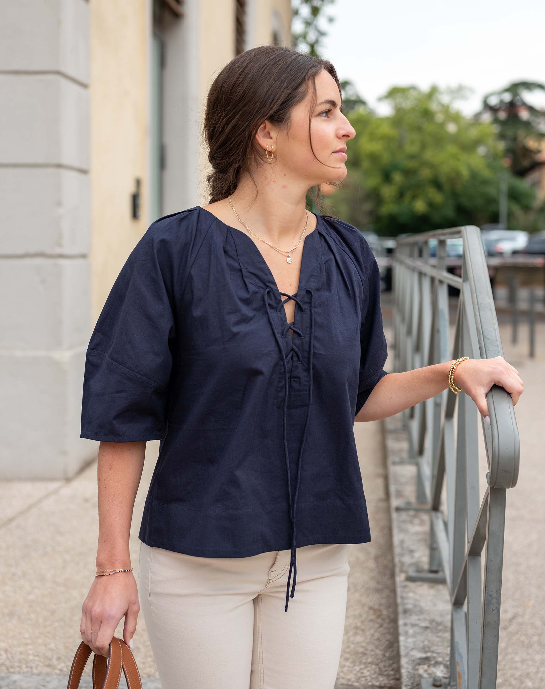 Woman wearing a navy blue blouse and beige pants standing outdoors.