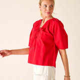 Woman wearing a red blouse with puff sleeves on a plain background