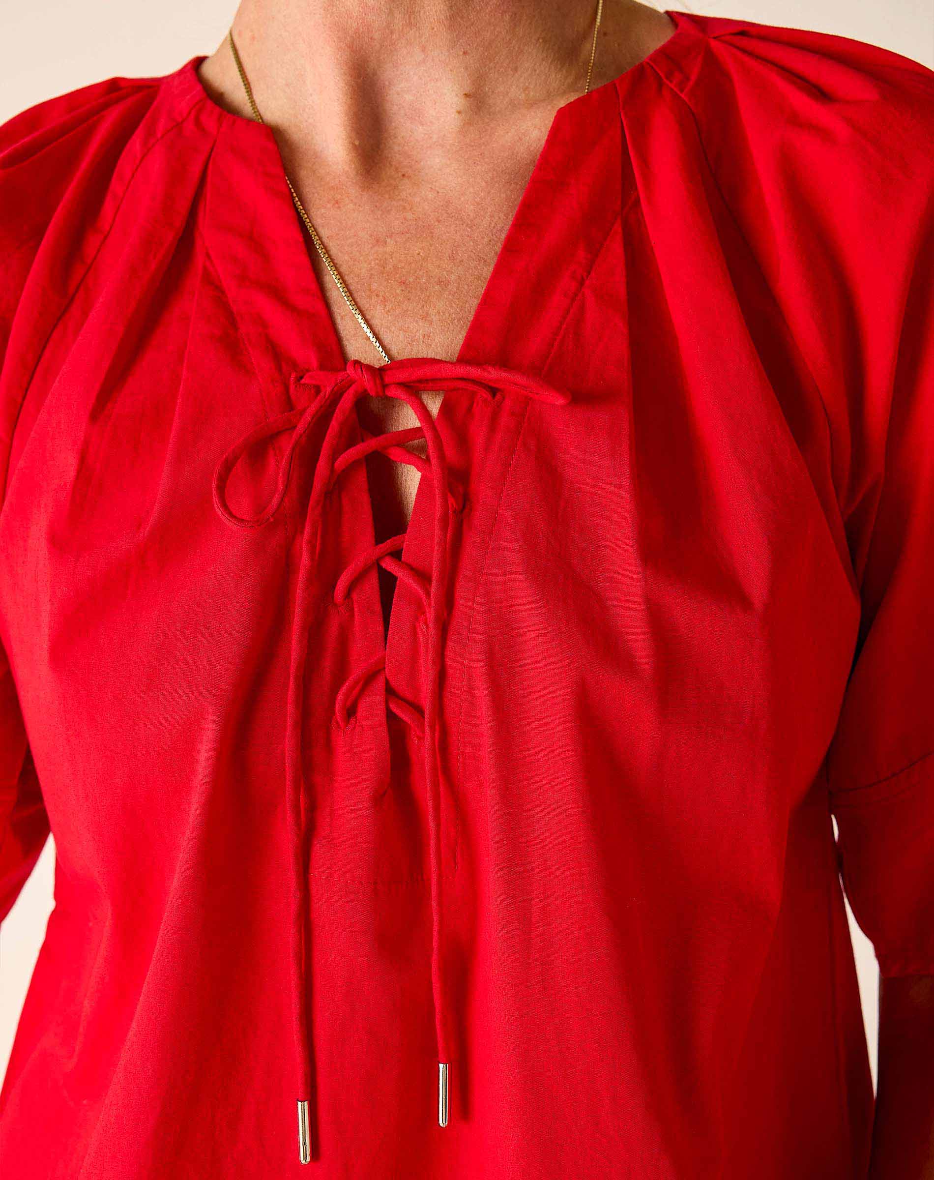 Red blouse with long sleeves and a tie detail on a neutral background