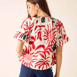 Woman wearing a red and white patterned top with denim shorts on a plain background
