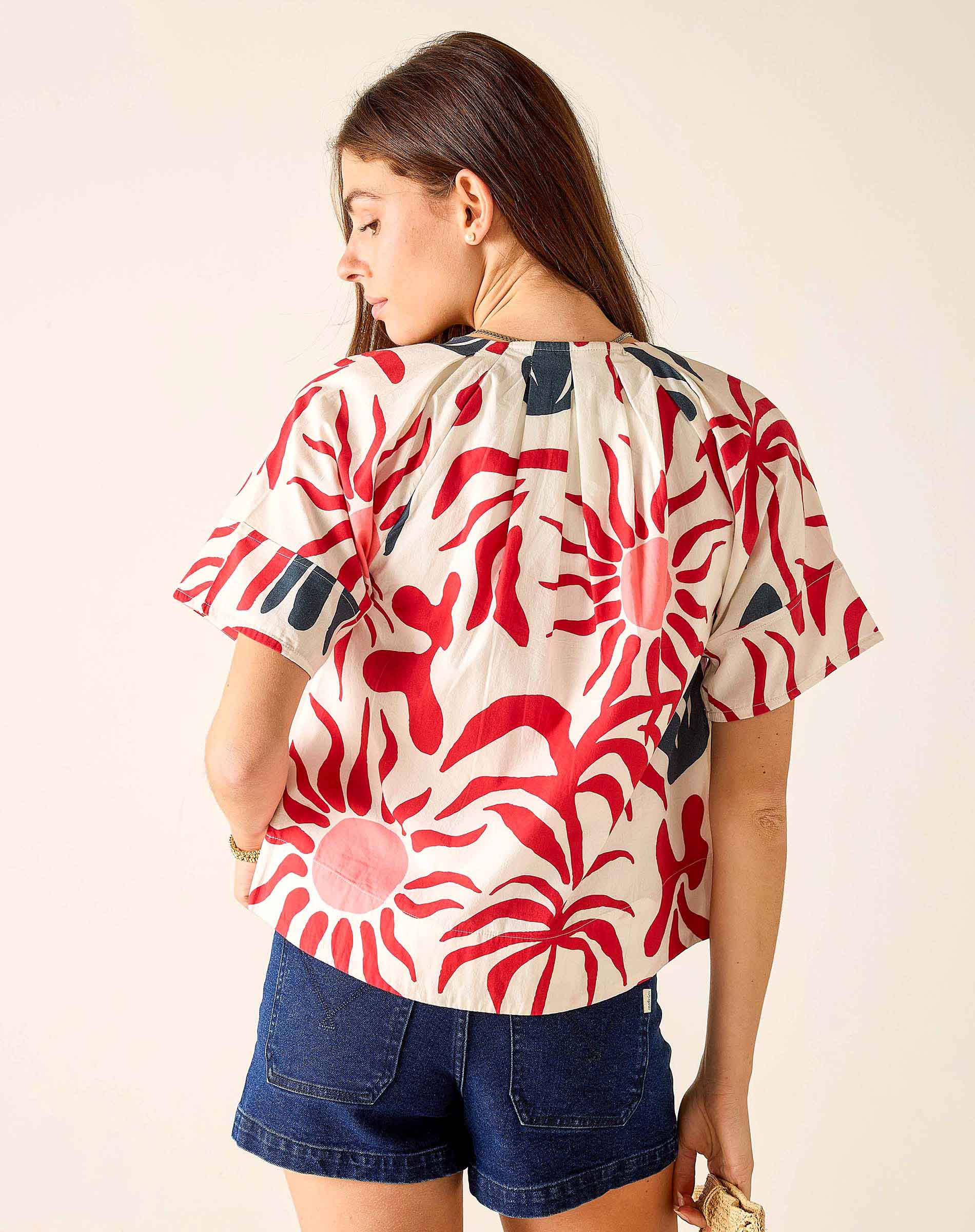 Woman wearing a red and white patterned top with denim shorts on a plain background