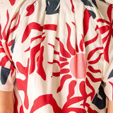 Close-up of a person wearing a patterned garment with red and blue designs on a beige background