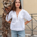 Woman wearing a white blouse and light blue jeans standing next to a palm tree.