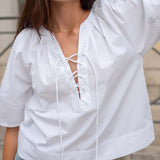 Woman wearing a white blouse with lace-up front and light blue jeans.