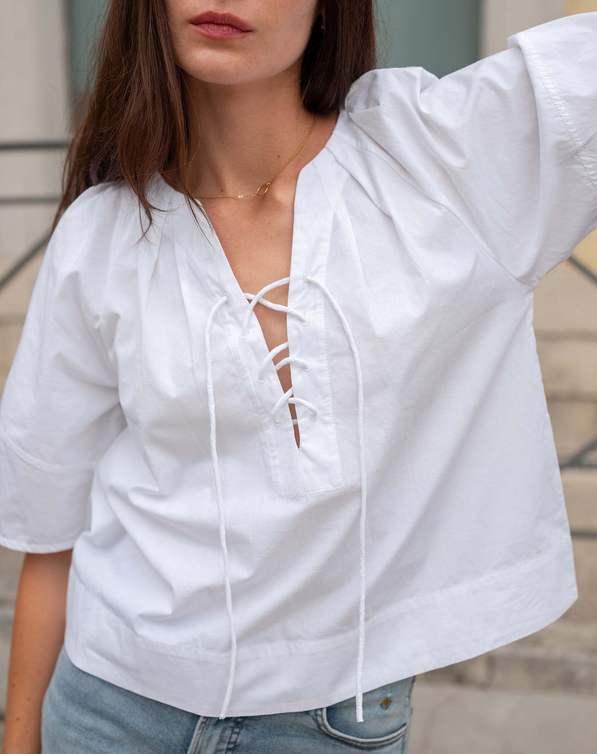 Woman wearing a white blouse with lace-up front and light blue jeans.