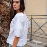 Woman wearing a white blouse and light blue jeans standing outdoors.