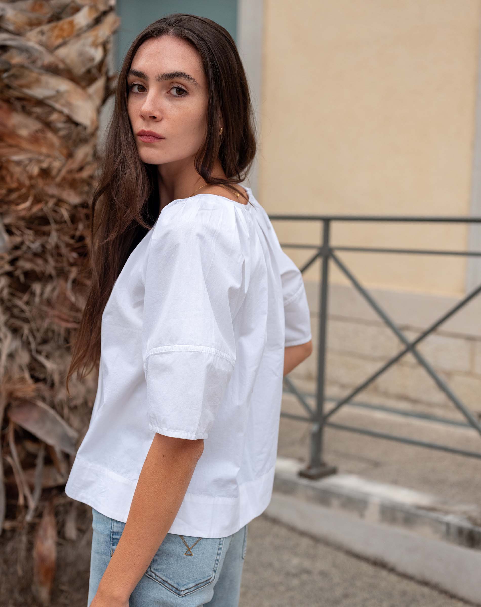 Woman wearing a white blouse and light blue jeans standing outdoors.