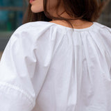 Person wearing a white blouse with puffed sleeves, blurred background