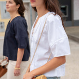 Woman in a white blouse holding a wicker bag with another person in the background.
