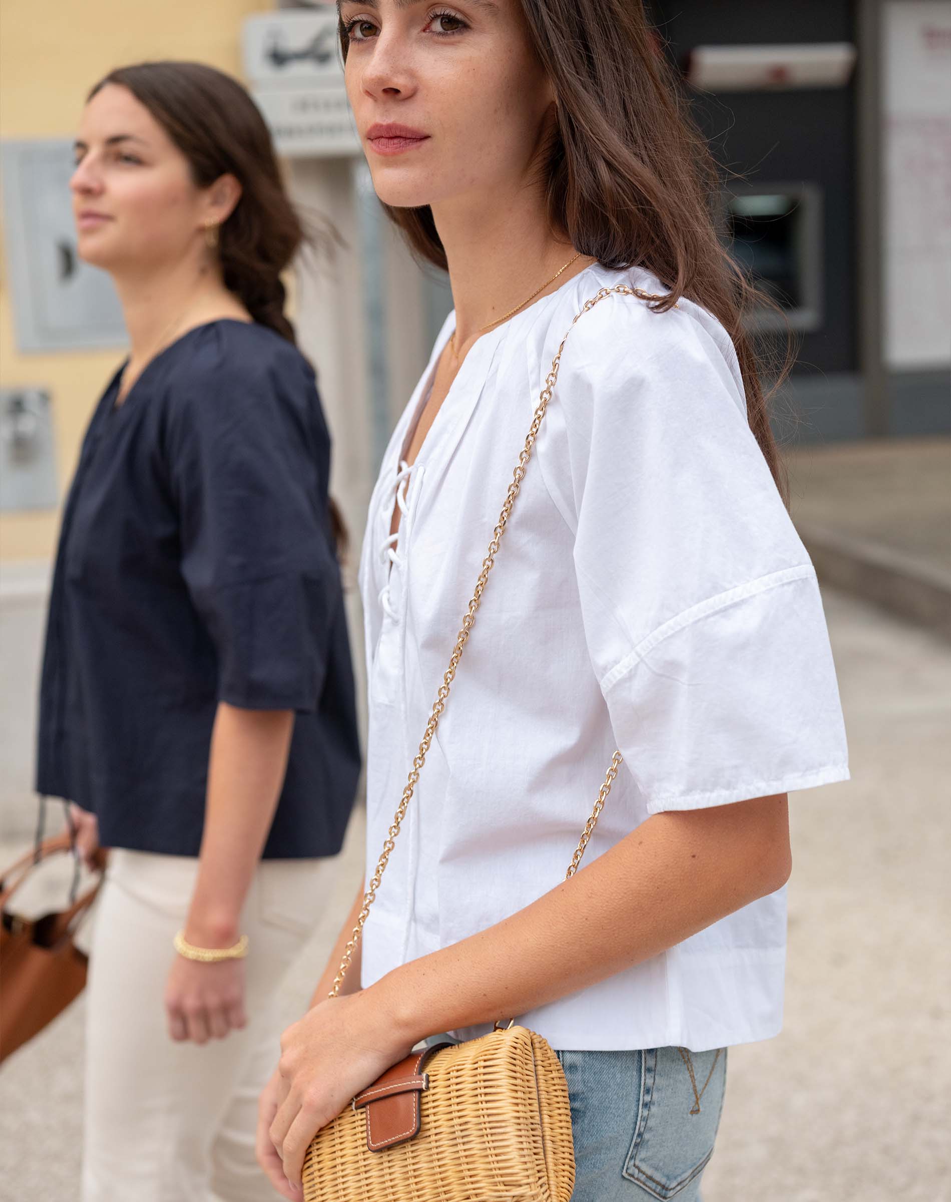 Woman in a white blouse holding a wicker bag with another person in the background.