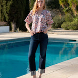 Multi-colored floral lace top with short sleeves and a buttoned front, paired with dark denim jeans.