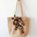 Woven bag with floral embroidery hanging on a wooden hook against a white wall.