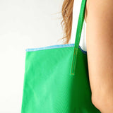 close up detail of woman holding le canvas tote in green with blue trim