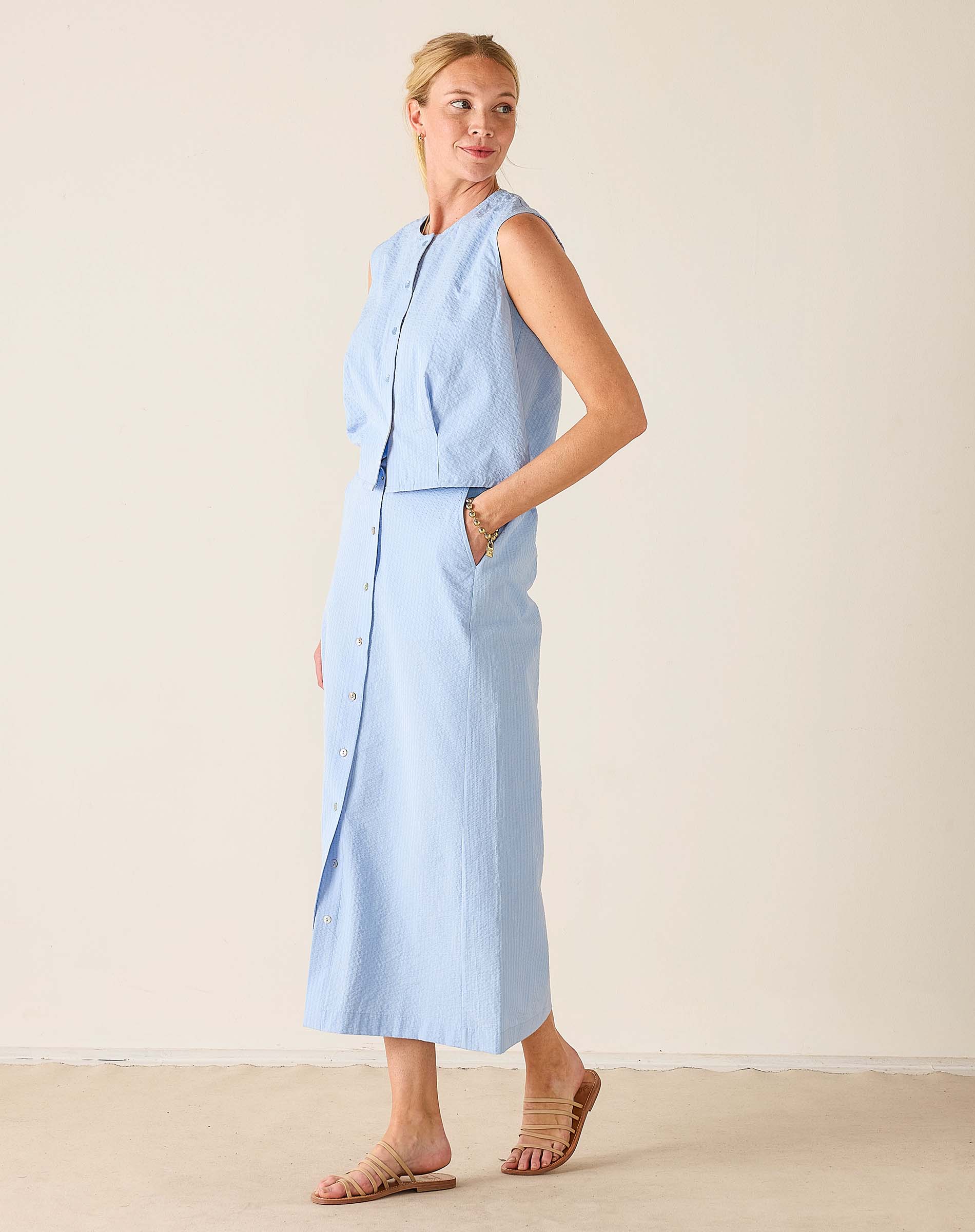 Woman wearing a light blue sleeveless top and pants set against a plain background