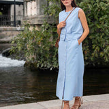 Woman in a light blue dress standing by a water feature with greenery.