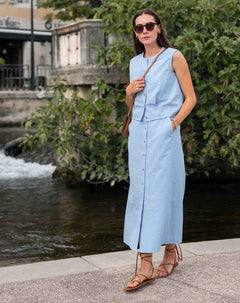 Woman in a light blue dress standing by a water feature with greenery.