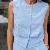 Person wearing a light blue sleeveless top with buttons, standing outdoors.