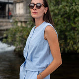 Woman wearing a light blue sleeveless top and pants by a water body.