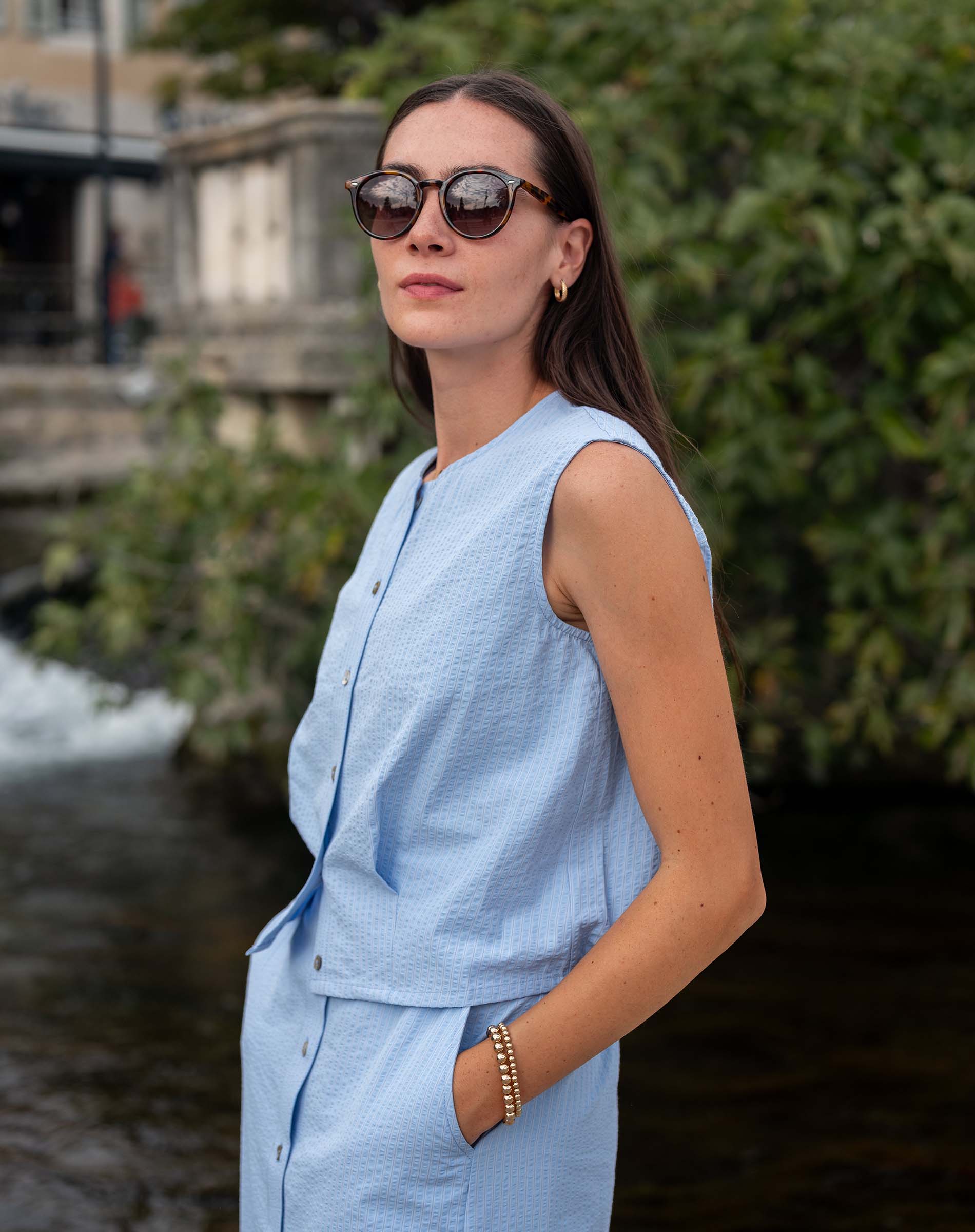 Woman wearing a light blue sleeveless top and pants by a water body.