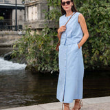 Woman in a light blue dress standing by a water fountain with greenery in the background