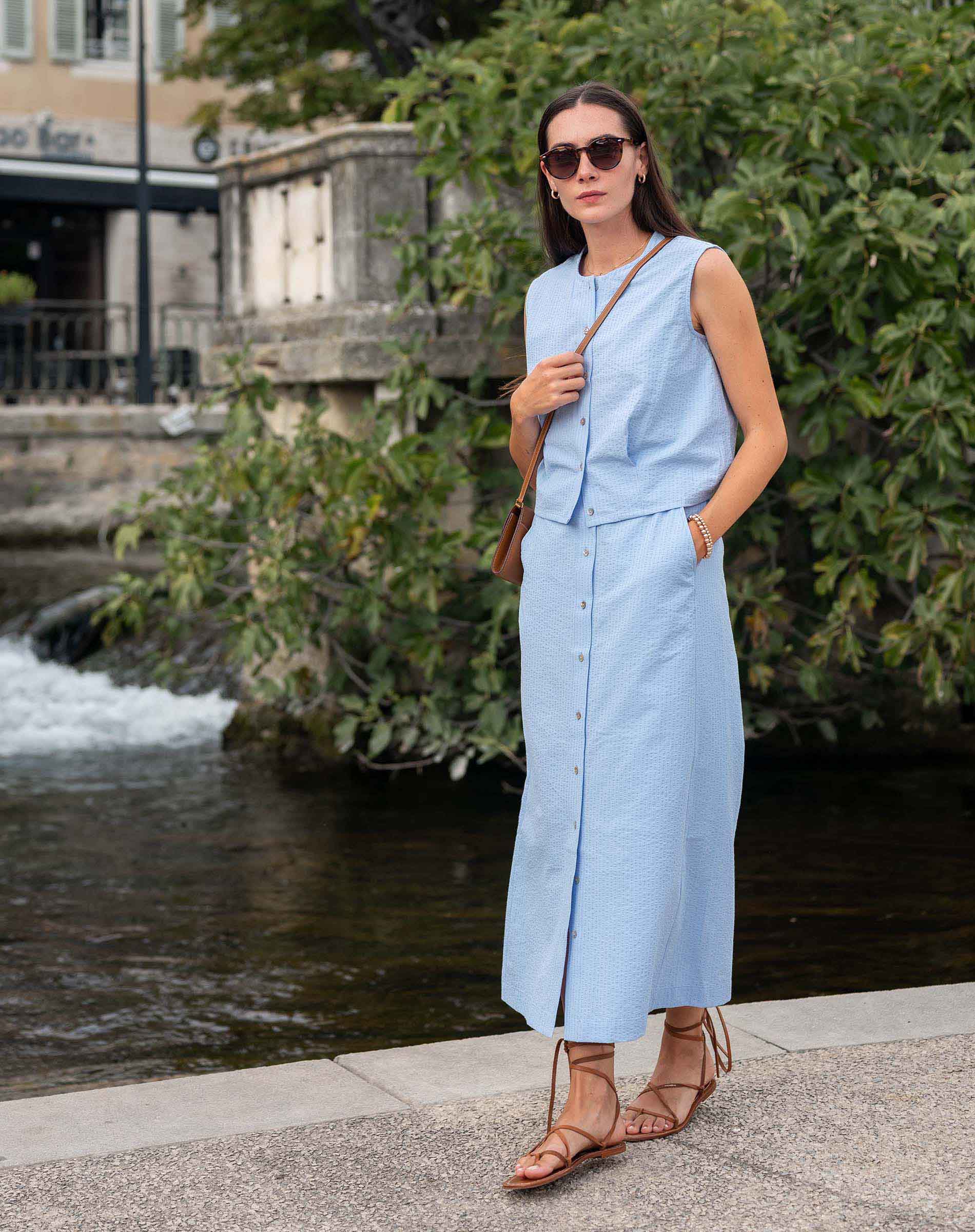 Woman in a light blue dress standing by a water fountain with greenery in the background