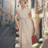 Woman in a beige dress standing on a street with buildings in the background