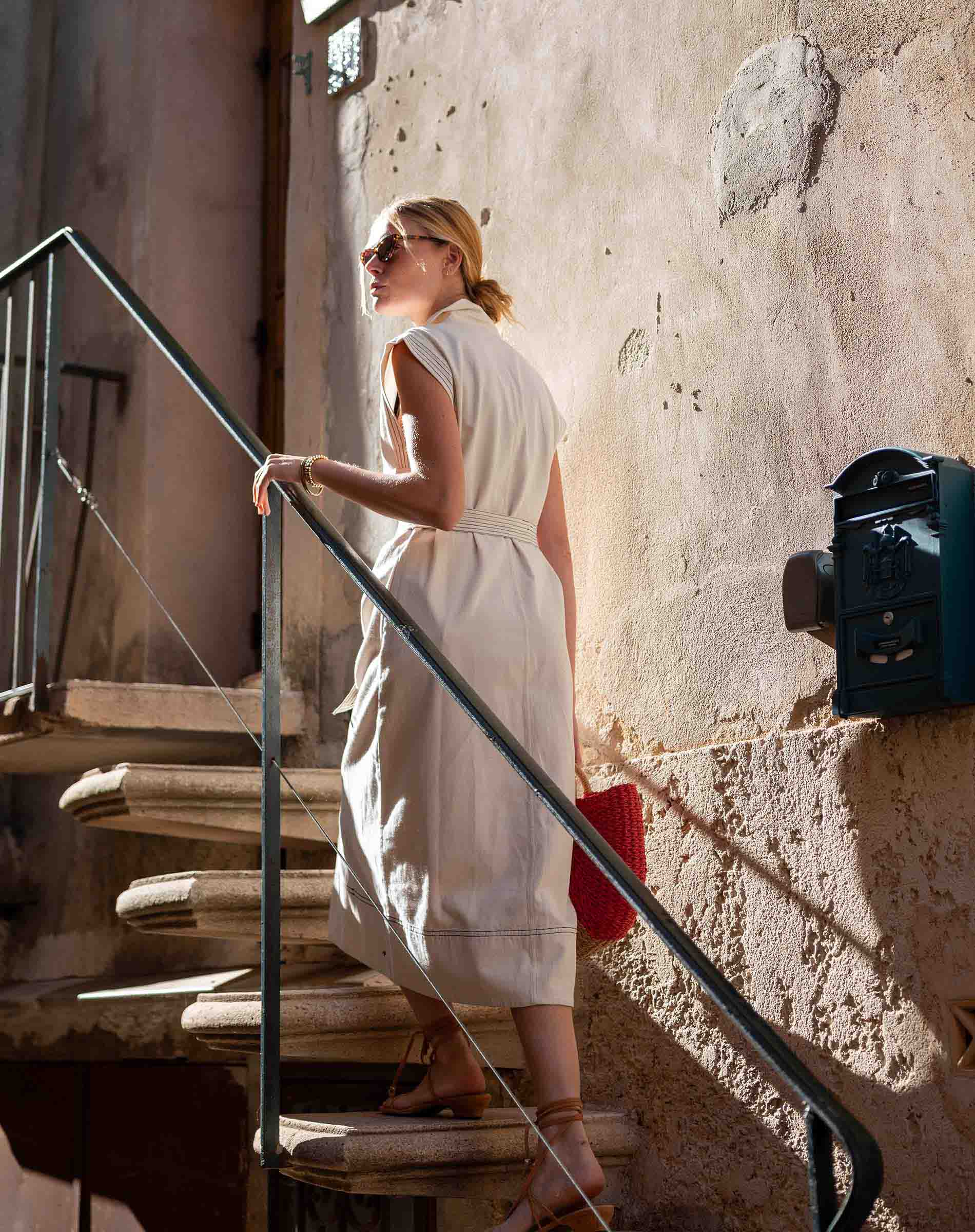 Woman in a white dress standing on a staircase with a textured wall behind her