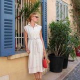 Woman in a white dress standing on a street with plants and a building in the background
