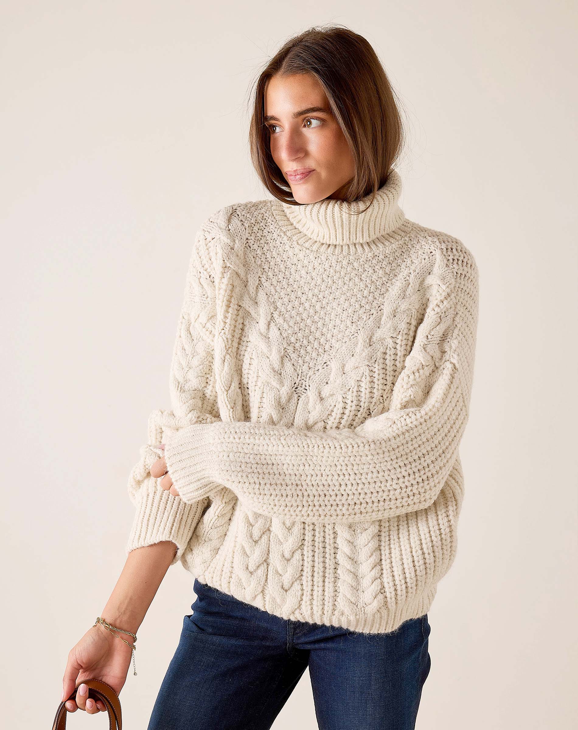 Ladies' travel-ready cream cable knit turtleneck sweater with a relaxed fit.