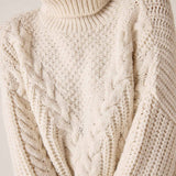 Cream cable knit turtleneck sweater with chunky ribbed neck and intricate stitch details.