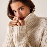 Cream cable knit turtleneck sweater with ribbed cuffs.