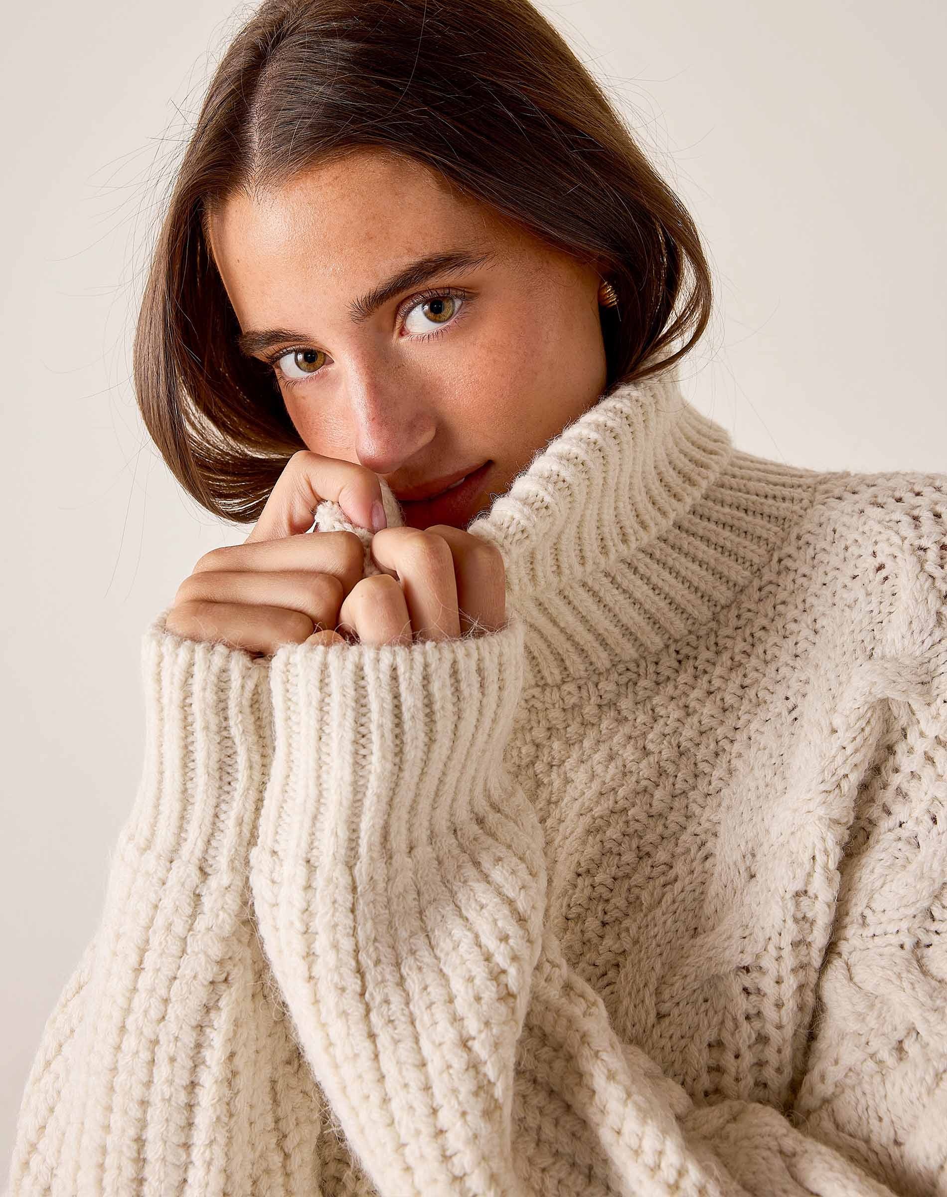 Cream cable knit turtleneck sweater with ribbed cuffs.