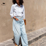 Woman wearing a white shirt and light blue jeans standing on a street.