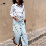 Woman wearing a white shirt and light blue jeans standing on a street.