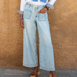 Person wearing light blue jeans and a white shirt against a beige wall.