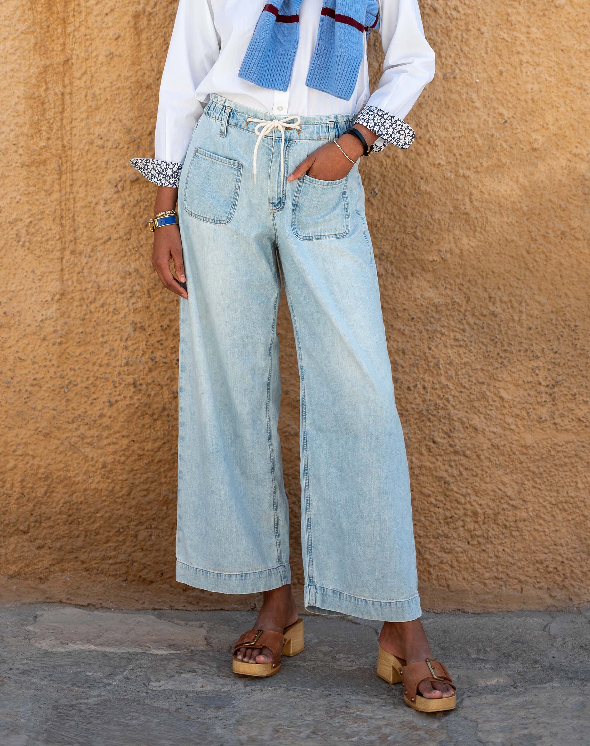 Person wearing light blue jeans and a white shirt against a beige wall.