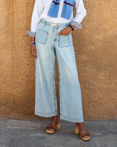 Person wearing light blue jeans and a white shirt against a beige wall.