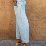 Person wearing light blue jeans and wooden sandals against a beige wall.